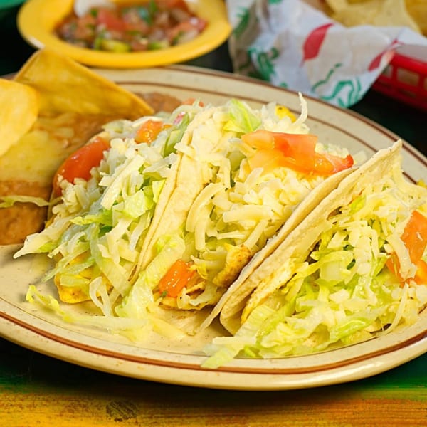 Three La Morena tacos filled with shredded lettuce, cheese, and diced tomatoes, with chips and salsa.