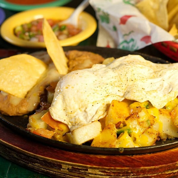 Mexican breakfast skillet with fried eggs, potatoes, cheese, and tortillas, served with salsa.